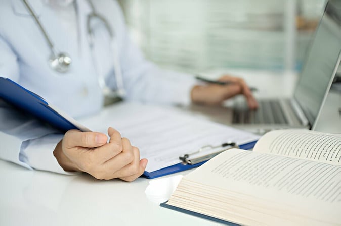 A healthcare professional reviewing documents on a clipboard for compliance and patient safety