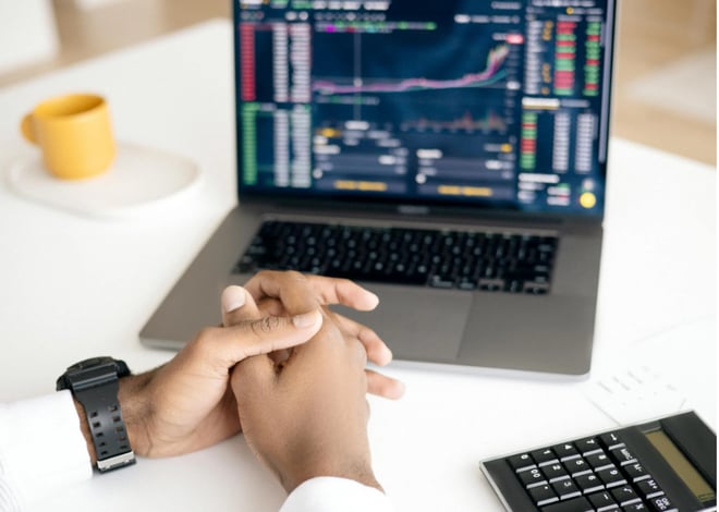 A person sitting in front of a laptop with a calculator signifying the importance of risk management in finance.