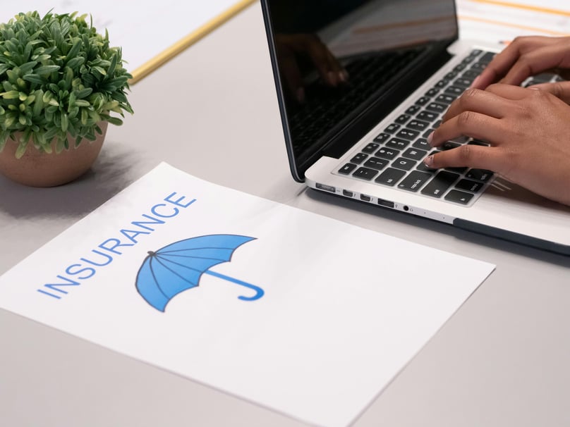 Insurance written on a paper beside a person typing on a laptop depicting predictive analytics in insurance industry