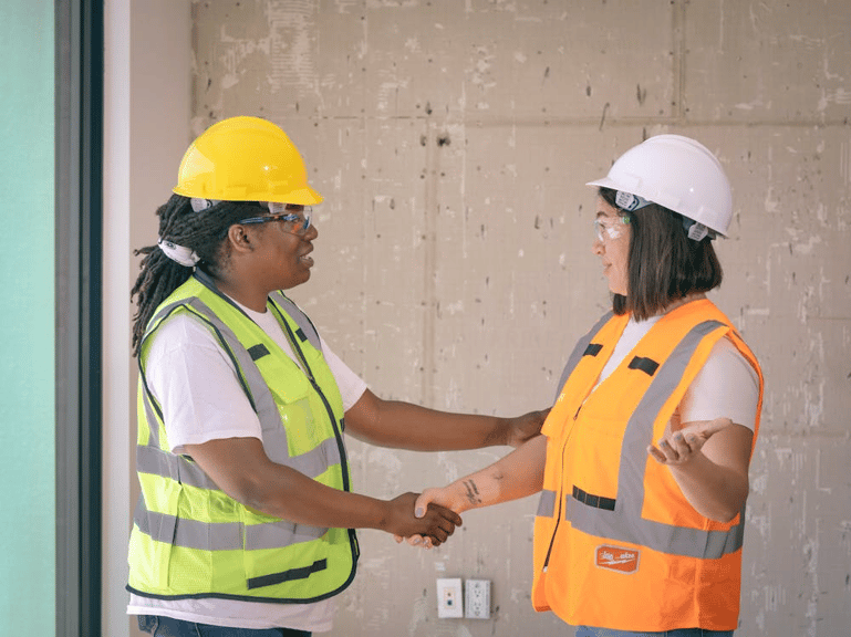 Construction workers in safety gear shaking hands, representing claims management systems improving compliance and resolution.