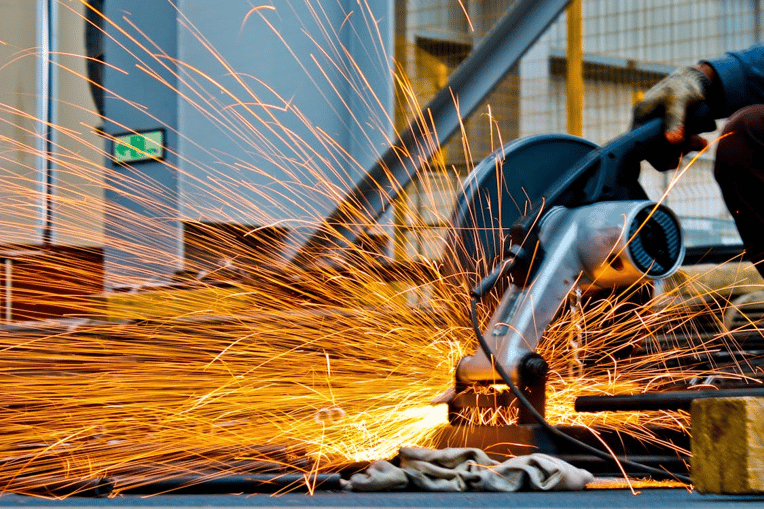 Worker using industrial cutting tool with sparks, symbolizing workplace risk and need for workers compensation software solutions