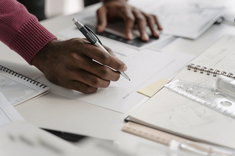 Professional drafting an implementation plan for a digital claims management system on paper with supporting notes and documents.