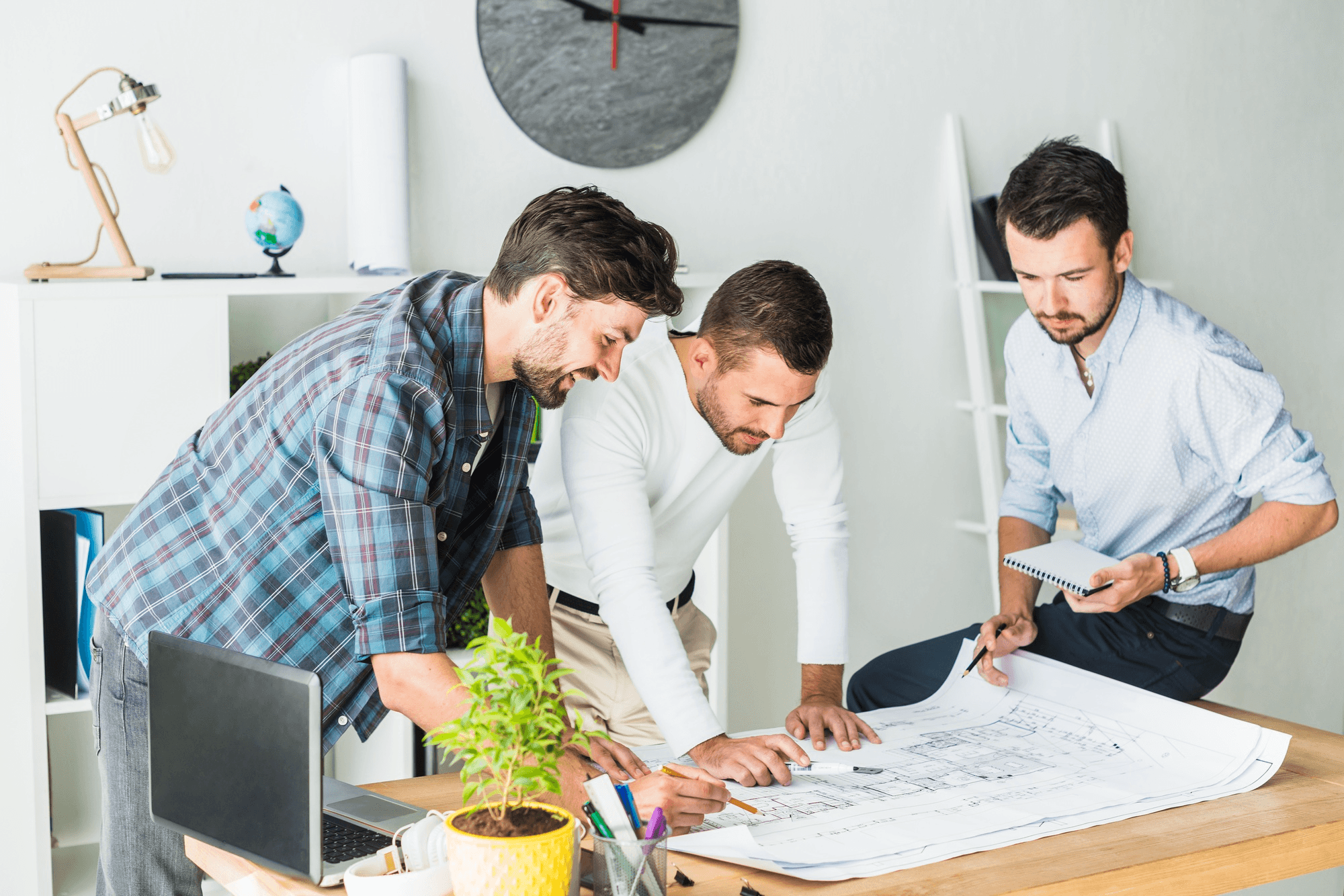 Three real estate professionals analyzing architectural blueprints in an office, discussing property risk management software